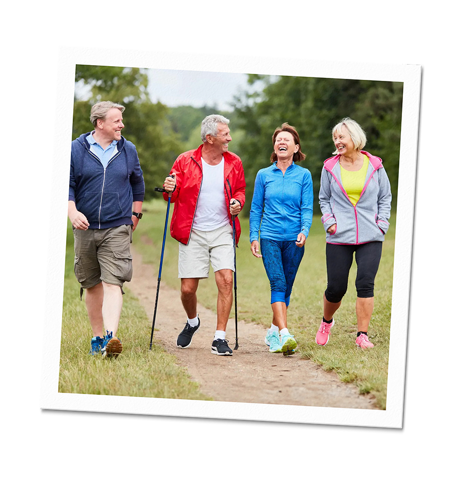 Four older adults walking and talking on a park trail.