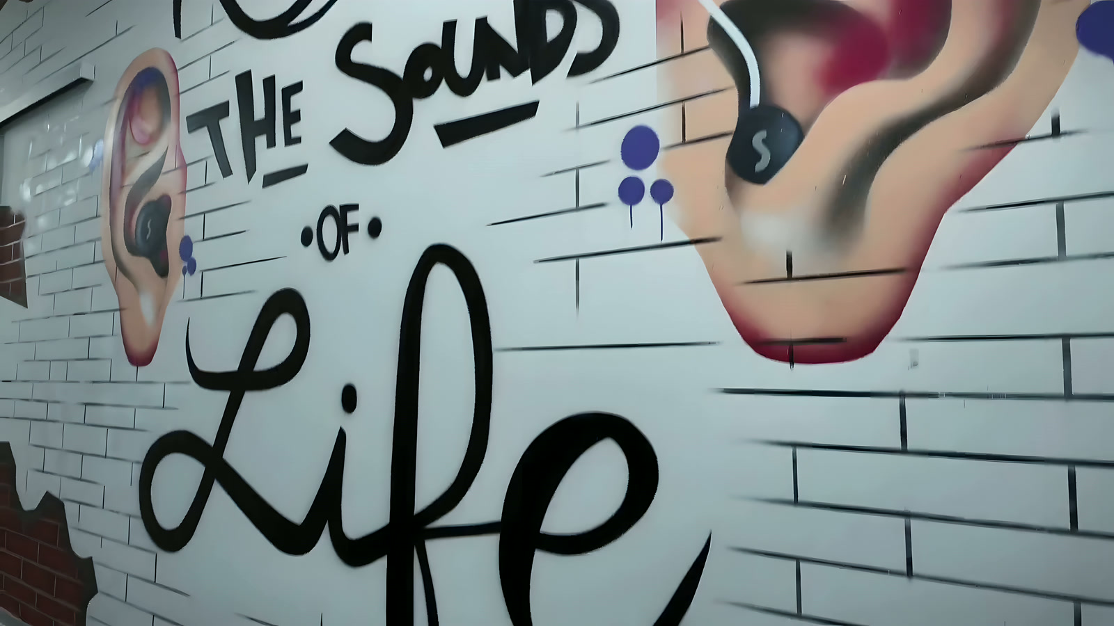 Street-art mural reading The sounds of life, with two painted ears.