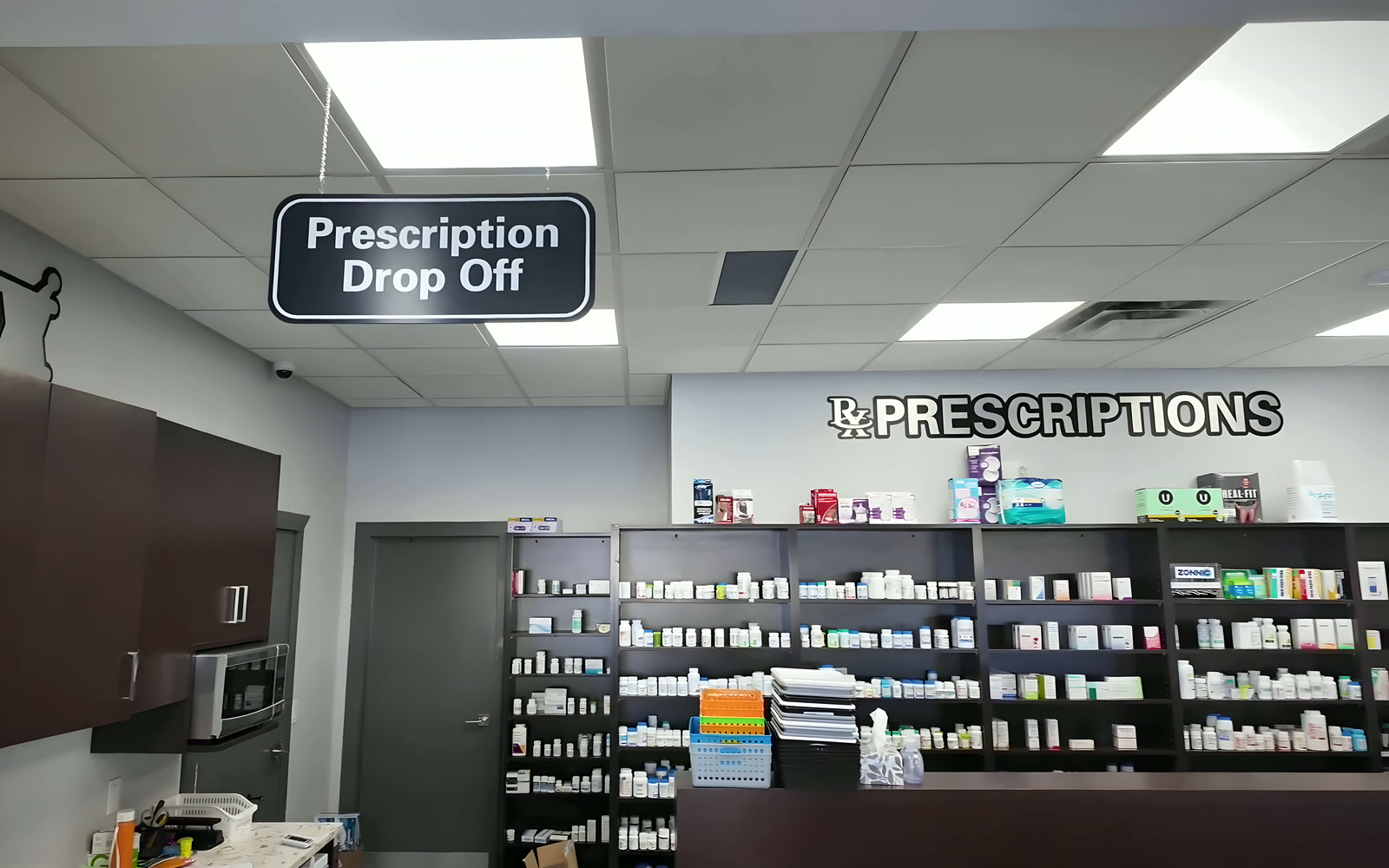The pharmacy counter with the Prescription Drop Off sign and shelves of medication.
